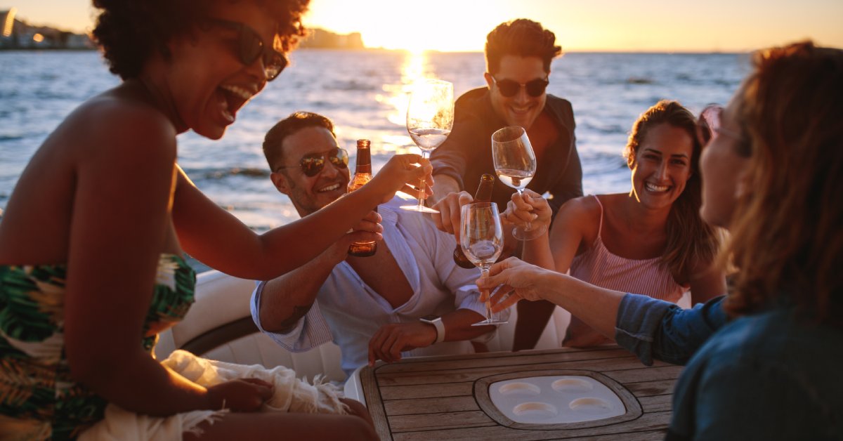 6 Things To Expect on Your Punta Cana Booze Cruise A group of adults sitting at a table on a boat, most of them holding wine glasses. Behind them is the water and the horizon.