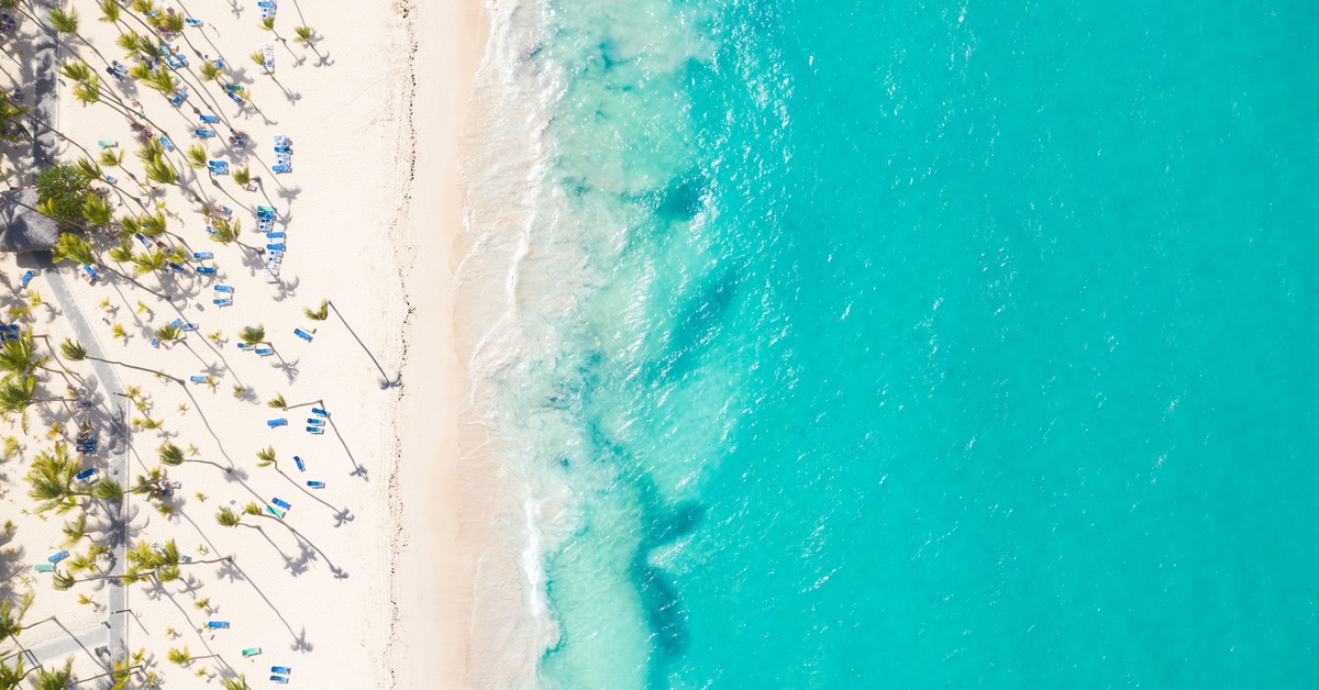 Best Time of Year To Book a Party Boat in Punta Cana Palm trees casting long shadows across a white sand beach with rows of blue lounge chairs near turquoise water.