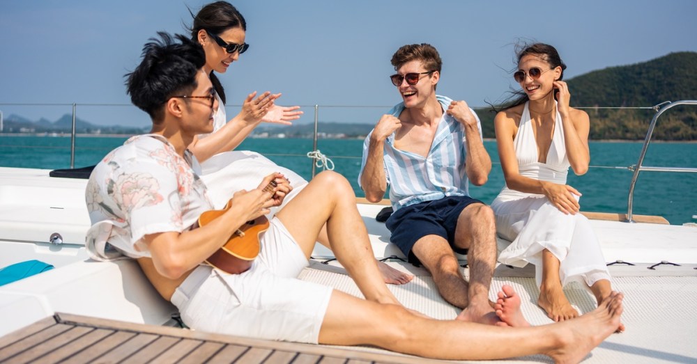 Four people chatting and laughing while sitting on a boat under a bright sunny sky near the sparkling water.