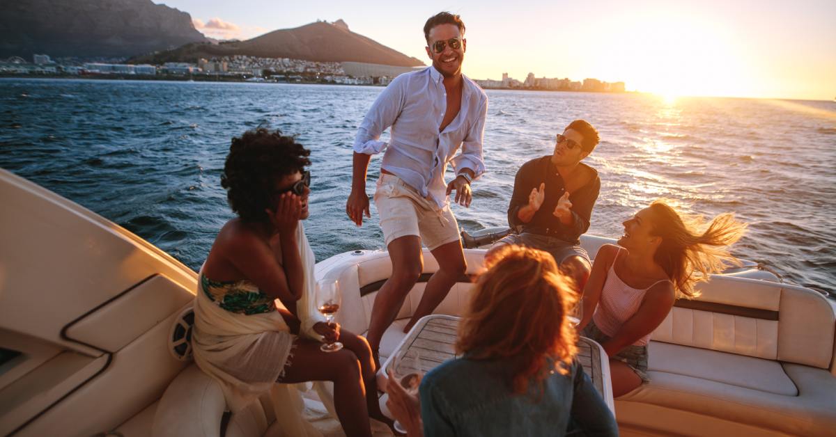 A group of people on a yacht during a sunset boat ride. There are mountains and a city coastline in the background.