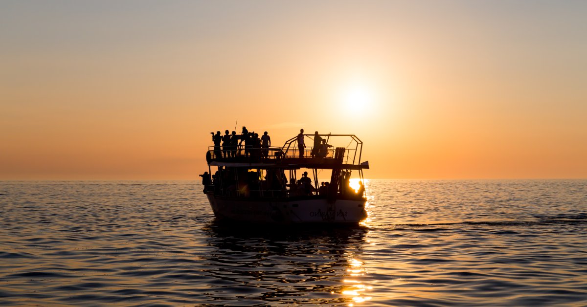 Silhouetted boat with people at sunset on calm sea.