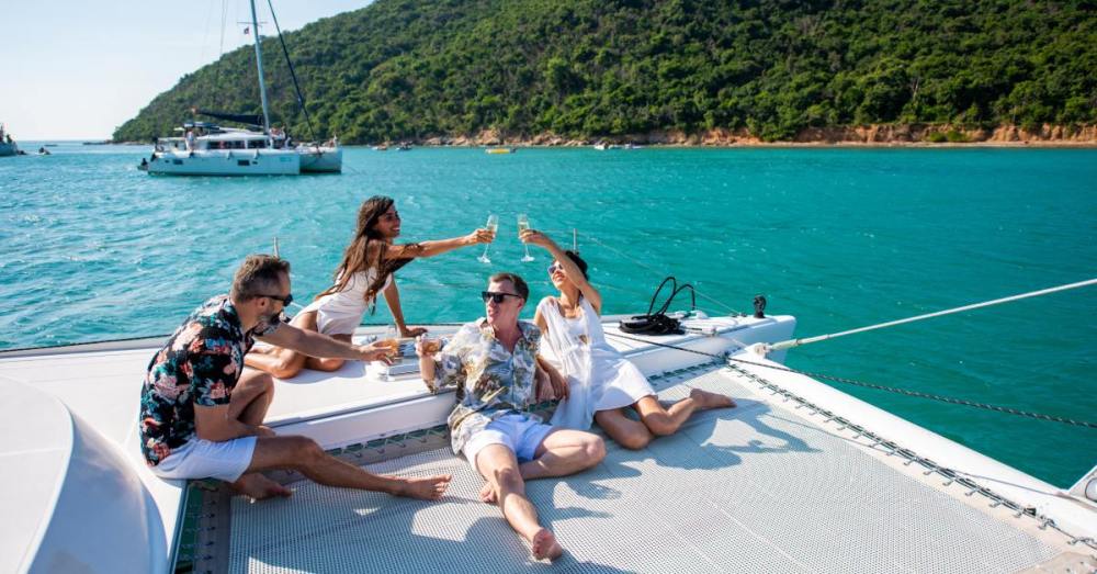 A group of two smiling men and two smiling women lounge on a large boat. They are toasting each other.