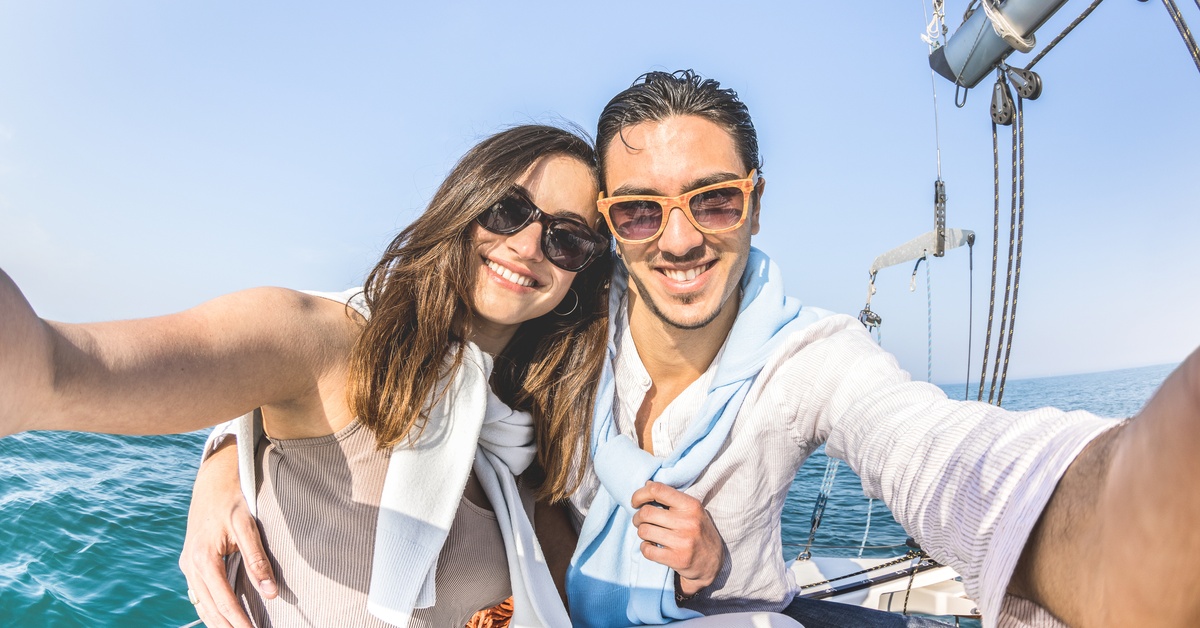 A young couple is smiling and posing to take a picture while on a boat. The boat is floating on the water.
