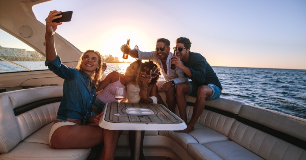 Three women and two men scrunch together around a table on a boat to take a photo. They are holding drinks.