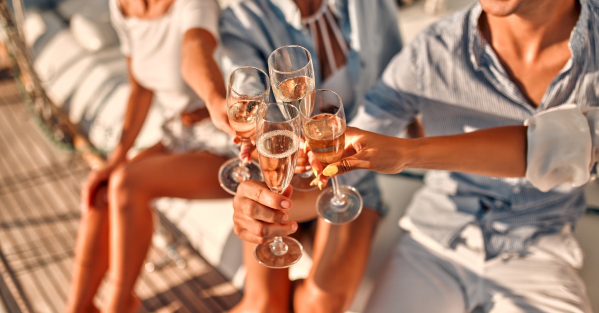 A close-up view shows people placing four champagne flutes filled with champagne in a circle for a toast on a party boat.